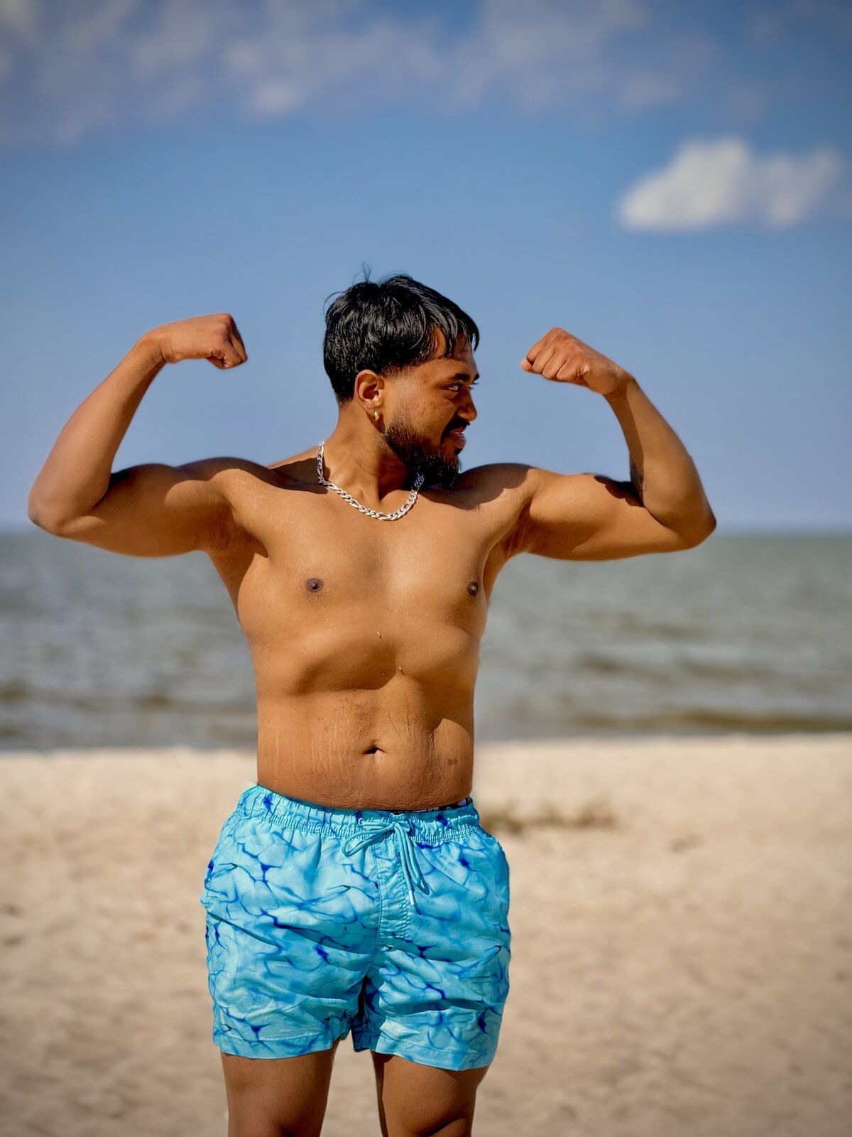 Hammer showing his strength progress, flexing both arms on the beach
